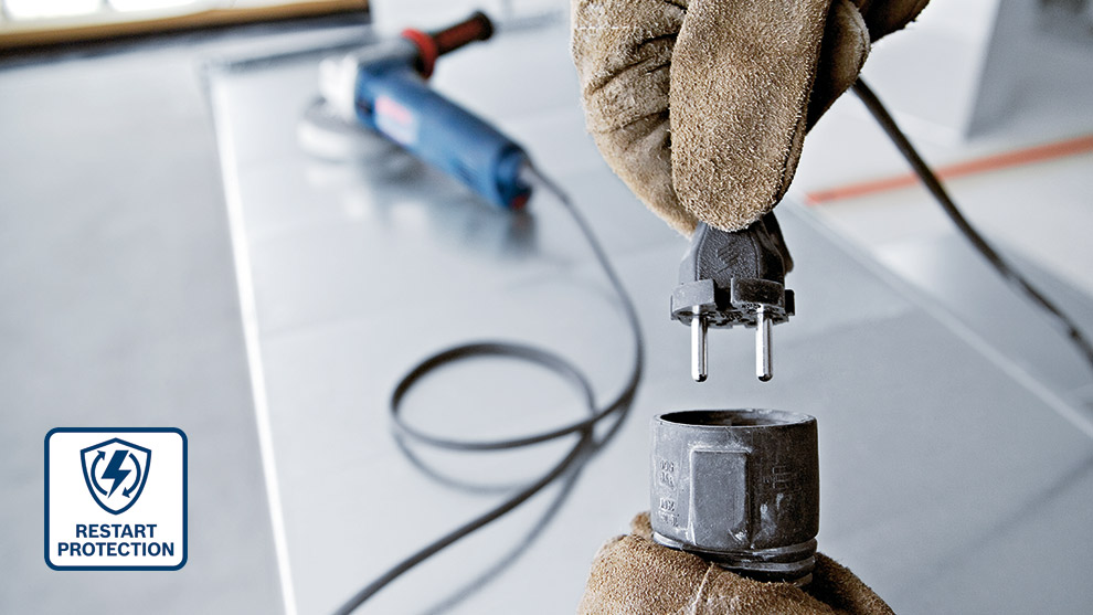 Restart Protection A hand in a glove connects a power plug to a tool on a work surface.