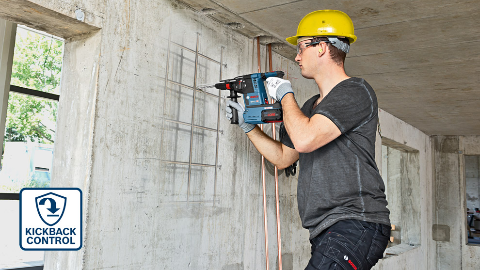 KickBack Control A worker drills into a concrete wall using a blue Bosch Professional tool, wearing a helmet.