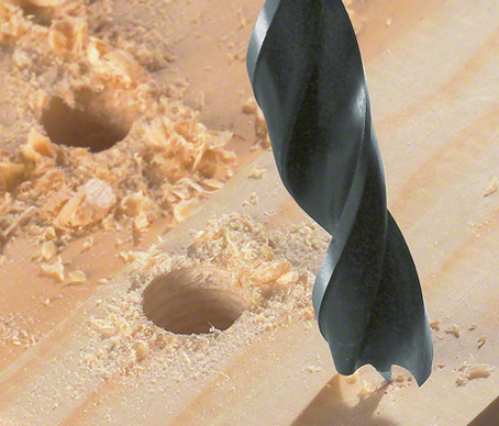 Drill bit making a hole in a wooden board with wood shavings scattered around.