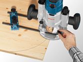 A person guides a plunge router along a curved line on a wooden board using a system accessory.