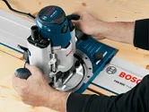 Person uses a plunge router on a wooden board with system accessories guide rail.