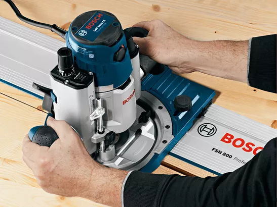 Person uses a plunge router on a wooden board with system accessories guide rail.