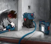 A person wearing safety equipment drills into concrete beside a corded dust extractor.