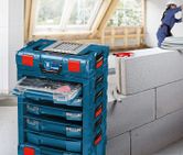 Stacked tool storage boxes with organized drawers beside a person wearing safety equipment.