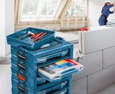 Stacked blue toolboxes with an open tray and drawer of assorted fasteners, person wearing safety equipment in background.