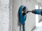 Drill with dust extraction accessory making a hole in a concrete wall.