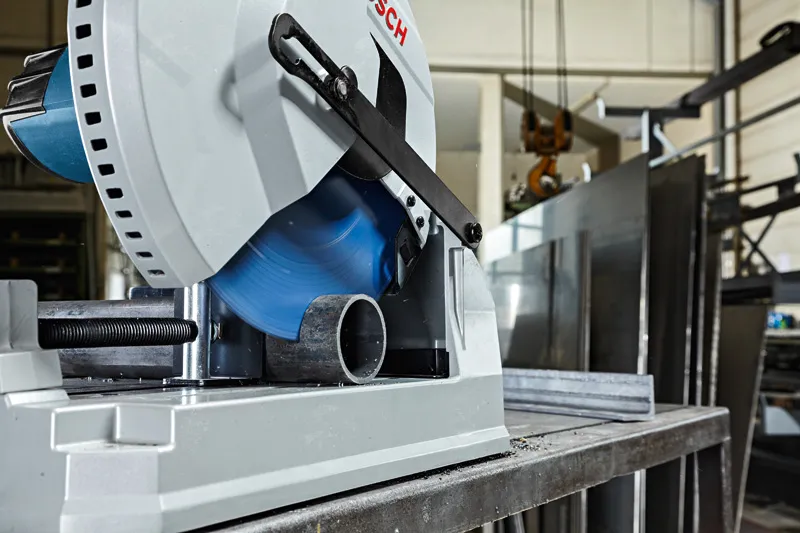 Metal cut-off saw slicing through a round metal pipe in an industrial workshop.