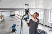 A person wearing safety equipment drills into a ceiling with a dust extraction system.