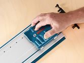 A person uses a blue system accessory on a metal rail set on a wooden surface.