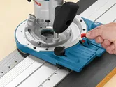 Person adjusts a blue router tool on a metal guide rail for precise woodworking.