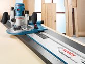 Power router guided along a metal track on a wooden work surface.