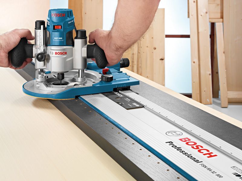 A person guides a wood router along a straight edge track on a light wooden surface.
