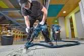 A person wearing safety equipment operates a demolition hammer to break tile flooring.