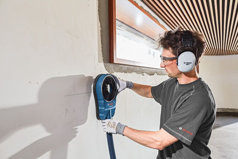 GDE 162 A person wearing safety equipment uses a wall-mounted dust extraction accessory.