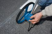 A person measures road distance with a blue measuring wheel on pavement.
