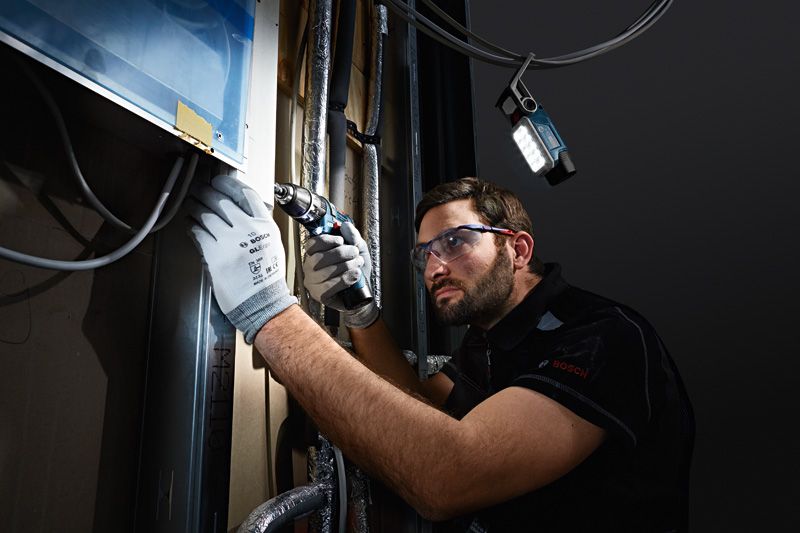 GLI 12V-330 A person wearing safety equipment drills into a wall, cordless light illuminating the workspace.