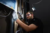 A person wearing safety equipment drills into a wall, cordless light illuminating the workspace.
