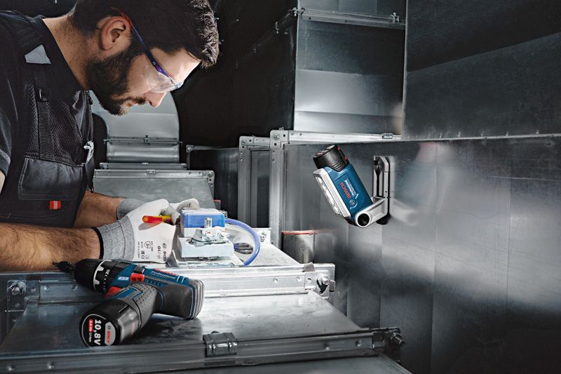 GLI 12V-330 A person wearing safety equipment works with electrical wiring under a cordless work light.