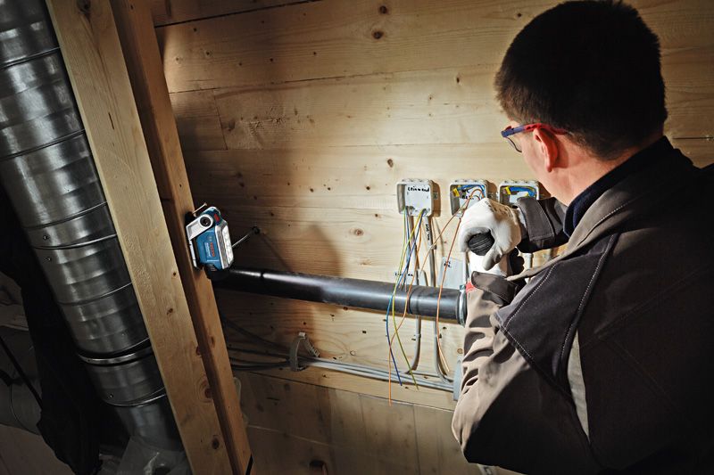 A person wearing safety equipment works on electrical wiring under bright cordless light.