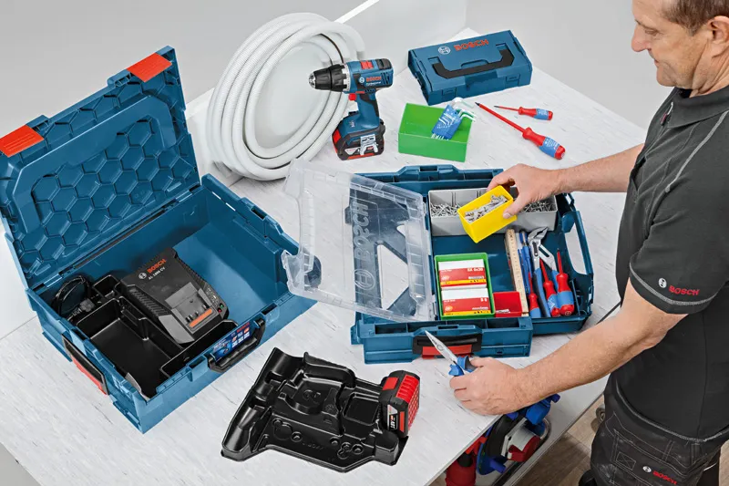 A person organizes screws and hand tools in a blue tool case on a workbench.