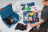 A person organizes screws and hand tools in a blue tool case on a workbench.