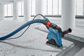 Wall chaser with dust extraction hose is cutting a groove in a concrete floor.