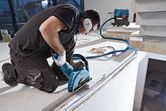 A person wearing safety equipment uses a wall chaser on concrete near a vacuum system.