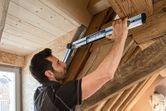 A person measures a wooden beam angle indoors using an angle measurer.