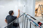 A person marks a wall using a digital inclinometer projecting a straight laser line.