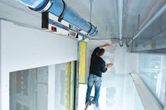 A person on a ladder marking a wall using a digital inclinometer for alignment.
