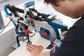 A person operates a sliding mitre saw to cut a board on a worktable.