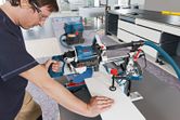 A person wearing safety equipment cuts wood with a sliding mitre saw in a workshop.