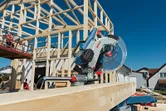 Sliding mitre saw positioned on a wooden beam at a house construction site.