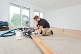 A person wearing safety equipment cuts laminate flooring with a sliding mitre saw.