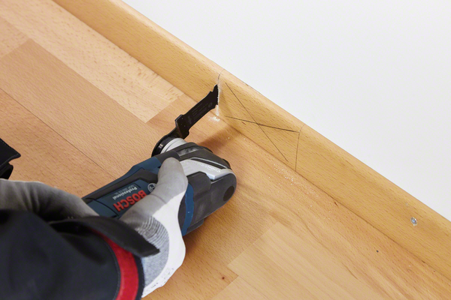 HCS plunge cut saw blade AIZ 32 EPC Wood Person wearing safety equipment cuts a wooden baseboard with a multitool.