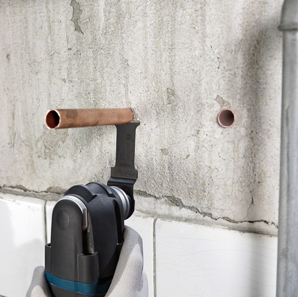 BIM plunge cut saw blade AIZ 20 AB Multi Material A worker wearing safety equipment cuts a copper pipe with a multi-tool near a concrete wall.