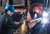 A person wearing safety equipment grinds metal on a large industrial rail car.