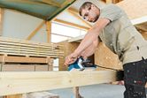 A person wearing safety equipment uses a planer to smooth a wooden beam in a workshop.