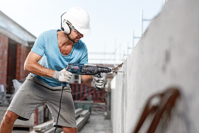 Hammer drill bit SDS plus-5 Person wearing safety equipment drills into a concrete wall on a construction site.