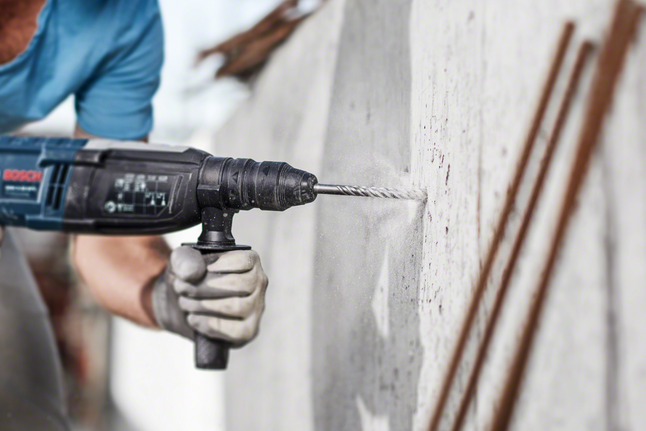 Hammer drill bit SDS plus-5 Person wearing safety equipment drills into a concrete wall.