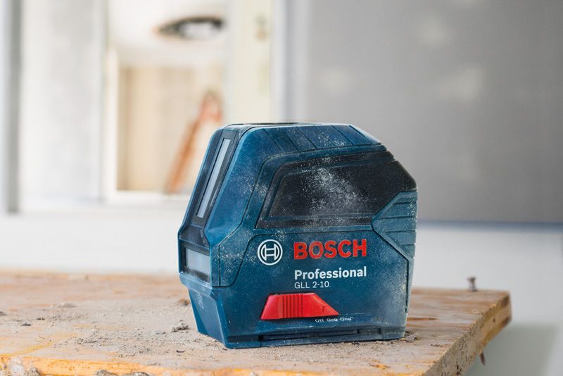 Laser leveling tool covered in dust on a wooden workbench in a construction area.