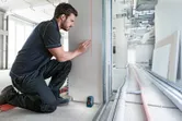 Person marking a wall using a laser leveling tool at a construction site.