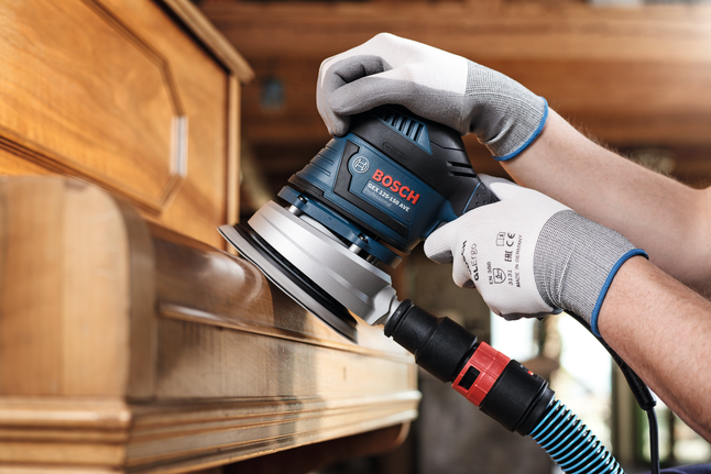 C430 sanding sheet, pack of 5 Person wearing safety equipment sands wooden furniture with a power tool.