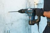 A person wearing safety equipment drills into concrete with a rotary hammer.