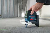 A person adjusts a laser leveling tool on a concrete floor in an unfinished hallway.