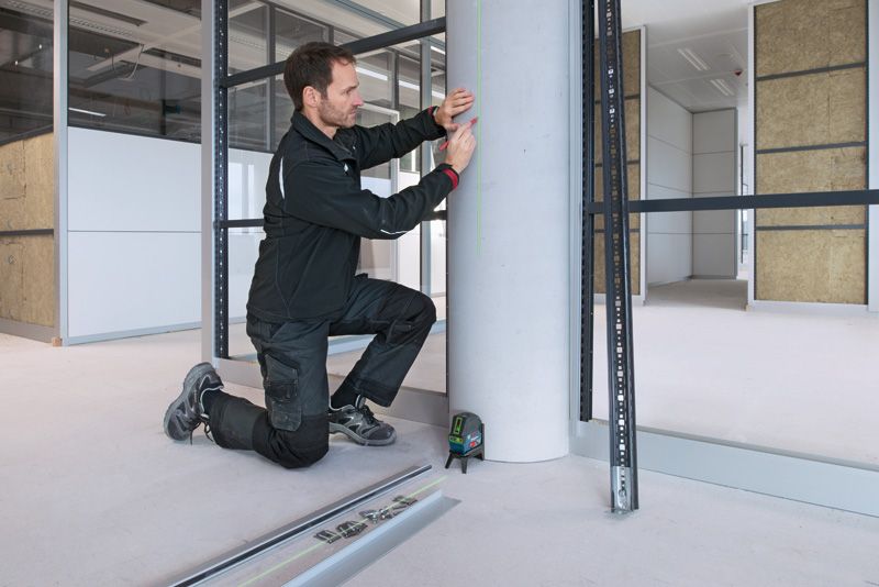 A person wearing safety equipment marks a concrete pillar using a laser leveling tool.