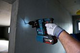 A person wearing safety equipment drills into a concrete wall in a dimly lit room.