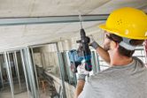 A person wearing safety equipment drills into a concrete ceiling during construction.