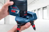 Person adjusts a laser leveling tool accessory in a bright, unfinished room.