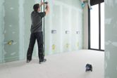 Person adjusting pipe on unfinished wall, green laser leveling tool projecting horizontal line.